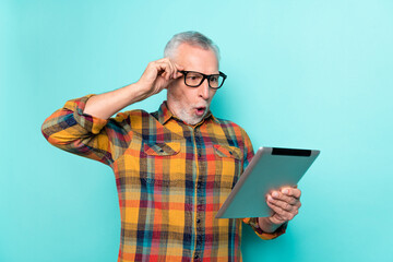 Poster - Photo of shocked retired man wear plaid shirt spectacles looking modern gadget isolated turquoise color background