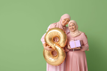 Poster - Muslim adult woman with her mother, gift box and balloon in shape of figure 8 on green background. International Women's Day celebration