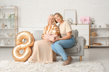 Canvas Print - Adult woman with her mother, gift box and balloon in shape of figure 8 at home. International Women's Day celebration