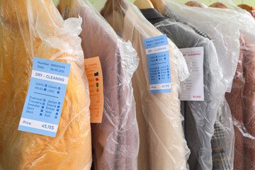 Poster - Rack with outwear in plastic bags after dry-cleaner's on green background, closeup