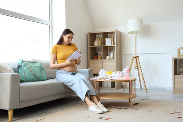 Wall Mural - Young pregnant woman with maternity hospital bag writing checklist on sofa at home