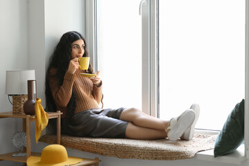 Sticker - Beautiful young woman with cup of hot tea near window at home