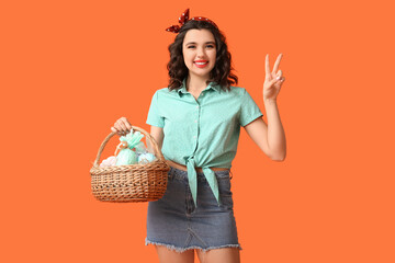 Sticker - Beautiful pin-up woman holding Easter basket and showing victory gesture on color background