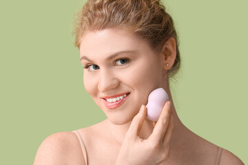 Wall Mural - Beautiful young woman with foundation on her face and makeup sponge against green background