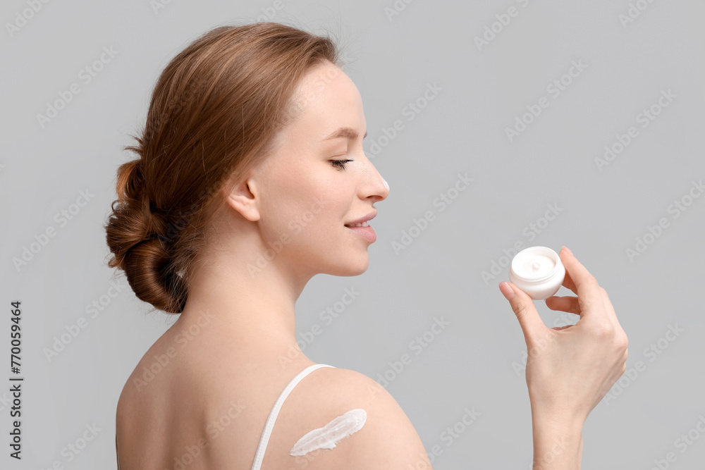 Young woman with jar of cream on grey background