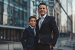 © Andrey Tarakanov - Confident father and son dressed in formal suits stand together against a backdrop of modern city architecture