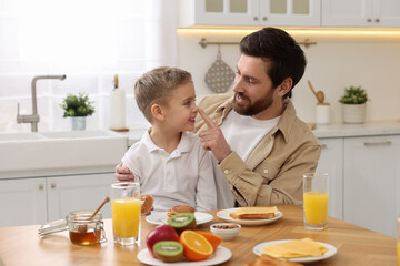 Canvas Print - Father and his cute little son having fun during breakfast at table in kitchen