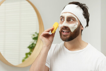 Poster - Man with headband washing his face using sponge in bathroom, space for text