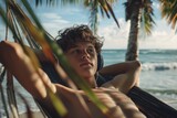 Fototapeta Miasto - Teen boy enjoying a calm moment in a beach hammock with headphones