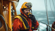 Deck Officer or Chief mate on deck of offshore vessel or ship , wearing PPE personal protective equipment - helmet, coverall. He holds VHF walkie-talkie radio in hands