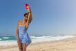 © ADDICTIVE STOCK - A woman enjoys capturing a breezy selfie by the ocean waves, their joy evident on a perfect, sunny beach day