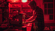 A laboratory technician meticulously adjusts dials on sophisticated equipment within the red glow of safety lights, indicating precision work in a technical or scientific setting.