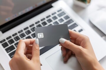 Close up of a woman's hands holding a gray credit card in front of a laptop computer