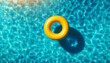 An aerial, overhead top down view of a yellow swimming pool ring float in a large expanse of crystal-clear blue water