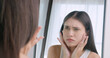 Young woman worried about the wrinkles on her face while looking in the mirror at home.