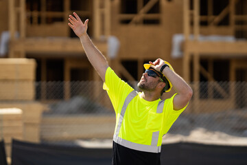 Wall Mural - Worker man on the building construction. Construction site worker in helmet work outdoors. Builder worker working on construction site. Worker pointing out.