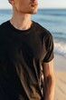 Ein junger Mann in schwarzem T-Shirt am Strand, T-Shirt Mockup 