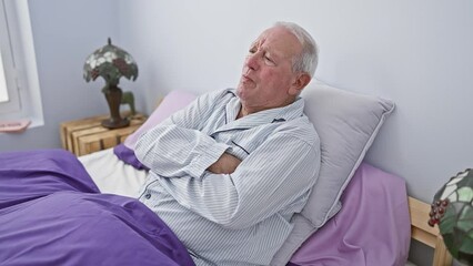 Canvas Print - Skeptic senior man, wearing pyjamas, with a nervous, disapproving expression on his face. he's crossed his arms in the bedroom, portraying a negative person.