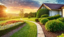 Country Lane In The Morning Natural Landscape Beautiful Manicured Lawn And Flowerbed With Deciduous Shrubs On Private Plot And Track To House Against Backlit Bright Warm Sunset Evening Light On Backgr
