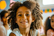 Cheerful young girl with curly hair smiling during classroom activities, surrounded by peers