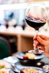 Sticker - A hand holds a red wine glass against a blurred dining setting, epitomizing fine dining and relaxation