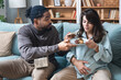 © Srdjan - Pregnancy support and fun. Young couple man and pregnant woman sitting at home teasing with sweet food forbidden by doctor. Male and female support and love during pregnancy period enjoy together.