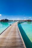 Fototapeta Zachód słońca - Maldives water villas paradise background. Tropical landscape, seascape with long pier, water villas, amazing sea sky and lagoon beach, tropical nature. Exotic tourism destination, summer vacation