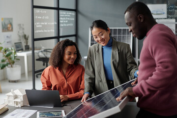 Aufkleber - Young African American businesswoman looking at model of solar panel while her colleagues presenting their project at working meeting
