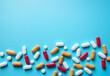 Top view of a group of medical drug capsules and pills of yellow, red and white colors on the blue background. Healthcare, pharmacy concept. Medical banner with copy space.