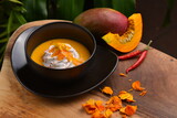 Fototapeta Sypialnia - Thai spicy pumpkin, mango and coconut milk soup with kaffir lime leaves , red chilli and galangal roots powder. Vegan, healthy food, gluten-free.