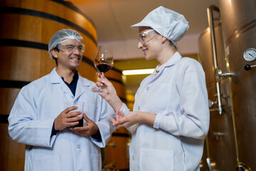 In a winery's aging room, a focused female wine expert evaluates the aroma of a wine sample while a male colleague observes.