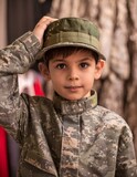 Fototapeta Uliczki - Courageous Cadet: Young Boy in Camouflage Uniform Holding Up Hat