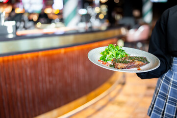 Sticker - A waiter serves a plate of grilled steak topped with fresh greens in a modern restaurant. The enticing moment captures the appeal of dining out and culinary artistry