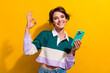 Photo of pretty nice young girl hold cellphone show okey symbol wear shirt isolated on yellow color background