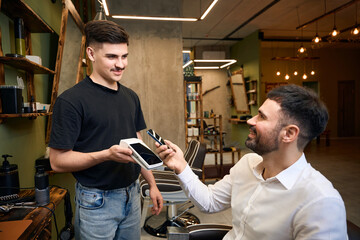 Client paying in barbershop with smartphone and pos terminal