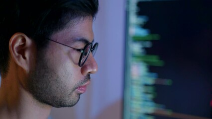 Wall Mural - close-up of a focused male programmer reviewing complex code on a computer monitor in a dimly lit ro