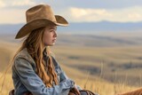 Fototapeta Konie - Contemplative young woman in cowboy hat gazing across rolling hills