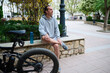 © Taras Grebinets - Caucasian young man sitting on a bench in the city, relaxing after cycling on electric bike. An e-bike on the foreground
