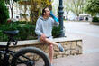 © Taras Grebinets - Full length male cyclist drinking water in the city. Electric motorbike, e-bike, electric bicycle bike on the foreground