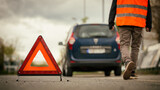 Fototapeta Perspektywa 3d - Warndreieck warnt vor Autopanne - Mann mit Warnweste im Hintergrund
