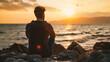Young man sitting on the rocks and looking at the sea at sunset