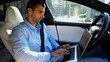 Handsome entrepreneur working on notebook while riding an autonomous self driving electric car at urban road. Male businessman typing text on laptop during riding on electrical vehicle with autopilot