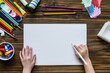 Child hand and blank white paper sheet with art supplies around on wooden table. Top view. Education, learning