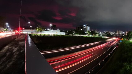 Wall Mural - Trail of light caused by vehicular traffic in Highway with buildings from downtown in the background, in Marília,