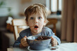 Young child with wide eyes sitting at a table, messily eating chocolate cereal with pieces of chocolate bar, with a smudged face indicating playful eating or a treat time