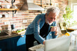 © Marko Geber - Senior man laughing while drinking juice and using laptop in kitchen