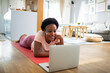 © Davor - Woman on yoga mat looking at laptop in living room