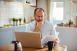 © Davor - Middle aged man holding bills using laptop at home