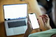 © Davor - Woman holding smartphone with blank screen in focus laptop in background
