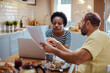 © Davor - Concentrated couple reviewing documents with laptop at kitchen table